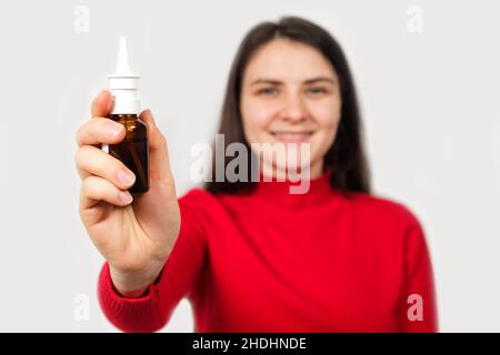 Eine brünette Frau in rot zeigt eine Flasche Nasenspray zur Behandlung von Rhinitis und Allergien Stockfoto