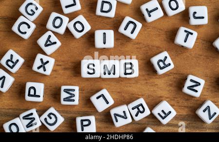 Kleine weiße und schwarze Perlenwürfel auf Holzbrett, Buchstaben in der Mitte buchstabieren SMB für kleine bis mittlere Unternehmen Stockfoto