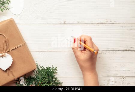 Weihnachtstisch mit Weihnachtsgeschenk. Handschrift der Frau auf einem Geschenkanhänger Stockfoto