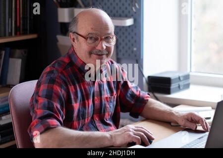 Älterer Mann mit Brille und Laptop zu Hause, der im Internet sucht Stockfoto