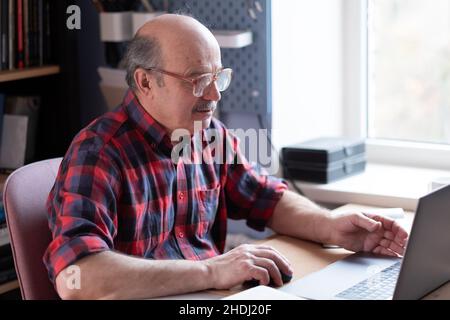 Älterer Mann mit Brille und Laptop zu Hause, der im Internet sucht Stockfoto