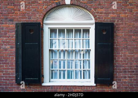 Traditionelles Bogenfenster mit schwarzen Fensterläden aus Holz an einer roten Backsteinmauer eines Mehrfamilienhauses Stockfoto