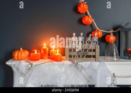 Halloween-Heimtextilien. Plastikspielzeug-Skelette in Holzkiste am Kamin vor einer dunkelblauen Wand. Eine Girlande aus Skeletten. Spinnennetz auf der Kommode. O Stockfoto