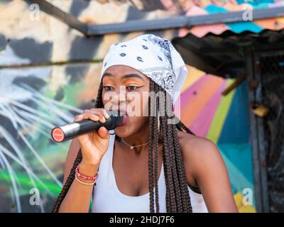 Medellin, Kolumbien - September 9 2021: Schwarze Rapper in Weiß mit Bandana, die in Mikrofon singt, in der Comuna 13, Touristische künstlerische Ur Stockfoto