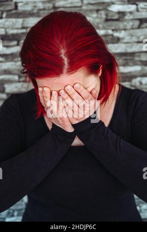 Eine verzweifelte Frau mit roten Haaren im Alter von 30-35 Jahren hält ihre Hände vor ihr Gesicht Stockfoto