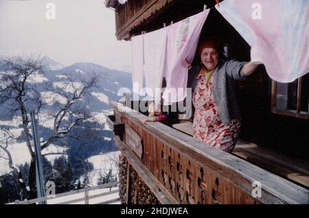 Ältere Dame, die ihre Wäsche online waschen lässt. Reife Frau hängt die Wäsche vor ihrem Haus in den alpen an der Linie. Frau schaut durch die Kleidung Stockfoto