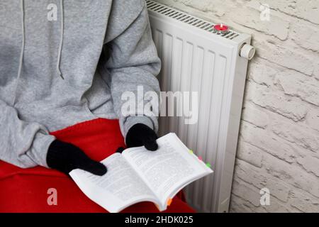 Der Besitzer in warmen Socken und Fäustlingen wärmt sich am Heizkörper auf. Harter Winter. Heizungskrise Stockfoto