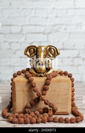 Bronzestatue von Lord Ganesha, dem hinduistischen Gott des Erfolgs. Rudraksha Rosenkranz für Meditation auf hellem Holzhintergrund und Yoga-Backstein. Stockfoto