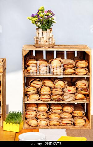 Street Food. Burger werden in Bastelpapier auf den Regalen einer Holzkiste eingewickelt. Stockfoto