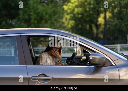 Weinendes junges Mädchen las Nachricht auf dem Handy. Frustriert verärgert junge Frau am Fahrersitz im Auto Stockfoto