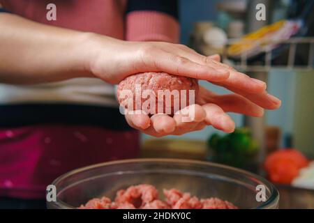 Nahaufnahme der Hände einer Frau, die Hackfleisch zubereitet, um Hamburger zu machen, das Fleisch ist immer noch roh und sie fügt die Zutaten, nette Atmosphäre in der Stockfoto