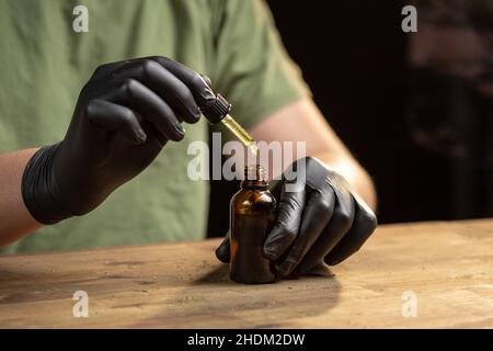 Hände tropfende CBD-Öltropfen in Glasflasche mit einer Pipette. Stockfoto