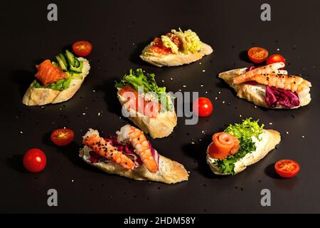 Verschiedene offene Sandwiches mit gesalzenem Lachs, Garnelen, Frischkäse, Salatblättern und Gurken. Meeresfrüchte, gesunde Lebensmittel. Schwarzer Stein Beton Hintergrund, Stockfoto