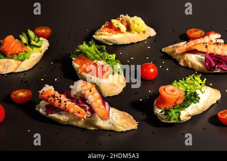 Verschiedene offene Sandwiches mit gesalzenem Lachs, Garnelen, Frischkäse, Salatblättern und Gurken. Meeresfrüchte, gesunde Lebensmittel. Schwarzer Stein Beton Hintergrund, Stockfoto