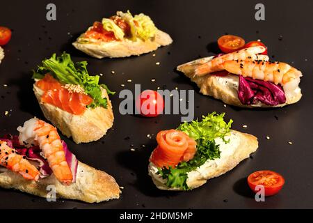 Verschiedene offene Sandwiches mit gesalzenem Lachs, Garnelen, Frischkäse, Salatblättern und Gurken. Meeresfrüchte, gesunde Lebensmittel. Schwarzer Stein Beton Hintergrund, Stockfoto