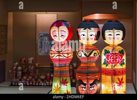 tokio, japan - 14 2021. oktober: Beleuchtete Papierlaternen, die japanische traditionelle handbemalte Kokeshi-Puppen darstellen, geschmückt mit Momiji-Blättern, Daruma fa Stockfoto