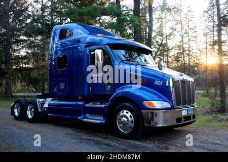 Glänzend blauer Peterbilt Sattelschlepper mit der untergehenden Sonne in der Ferne. Stockfoto