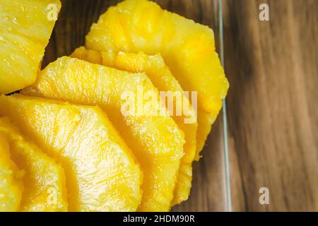 Nahaufnahme der Hände einer jungen Frau, die mit einem Kochmesser auf einem Holztisch in einer Küche eine saftige Ananas schneidet. Stockfoto