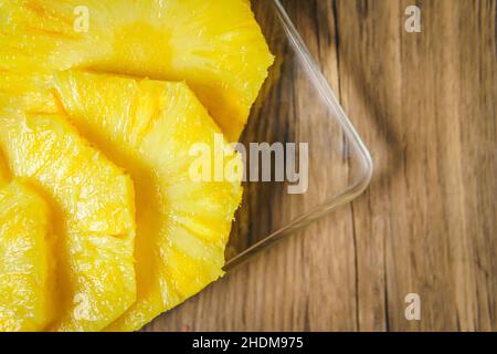 Nahaufnahme der Hände einer jungen Frau, die mit einem Kochmesser auf einem Holztisch in einer Küche eine saftige Ananas schneidet. Stockfoto