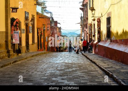 Sonnenuntergang auf einer belebten Kopfsteinpflasterstraße im El Centro neben dem El Jardin mit Geschäften und Cafés in der Kolonialstadt San Miguel de Allende, MX Stockfoto