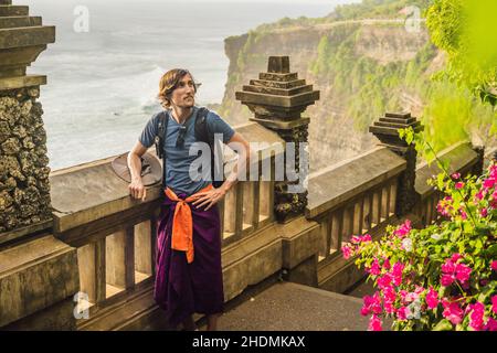 Junger Mann, der im Pura Luhur Uluwatu Tempel, Bali, Indonesien, unterwegs ist. Atemberaubende Landschaft - Klippe mit blauem Himmel und Meer Stockfoto