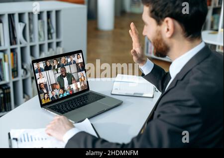 Ein erfolgreicher Mann, der einen Laptop verwendet, führt ein virtuelles Meeting mit Geschäftspartnern in einem Videoanruf durch. Eine Gruppe verschiedener, multirassischer Geschäftsleute auf dem Laptop-Bildschirm, die eine Videokonferenz abhalten Stockfoto