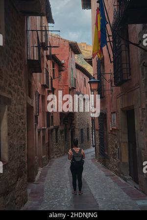 Schöne Aussicht auf ein Mädchen, das in einer Steinfußbodenstraße zwischen alten Gebäuden in Albarracin, Spanien, läuft Stockfoto