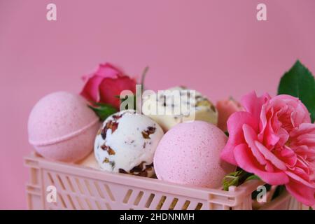 Badebomben und Trüffel mit Rosenblättern in einer rosa Schachtel auf einem rosa Hintergrund.Badebomben mit Rosenextrakt.Schönheit und Aromatherapie. Bomben Im Blumenbad Stockfoto