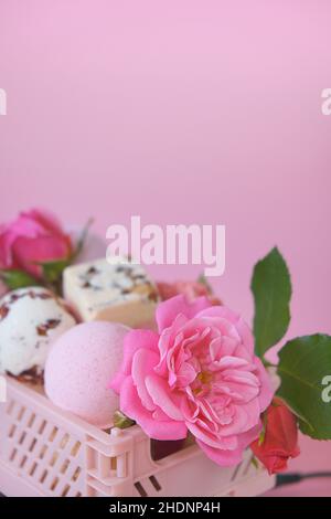 Kosmetik mit Rosenextrakt. Badebomben und Trüffel mit Rosenblättern in einer rosa Schachtel in Nahaufnahme auf einem rosa Hintergrund.Badebomben mit Rosenextrakt.Schönheit Stockfoto