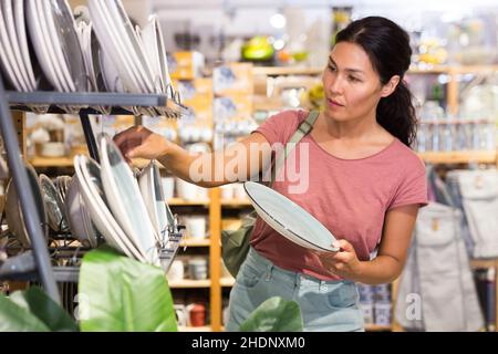 Positive weibliche Käufer wählt neue Teller im Geschirrladen Stockfoto