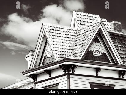 Graustufenaufnahme eines alten Hauses mit Ziegeldach unter einem bewölkten Himmel Stockfoto