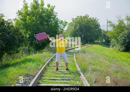Glücklicher Mann mit rotem Koffer, der auf der Eisenbahn springt Stockfoto