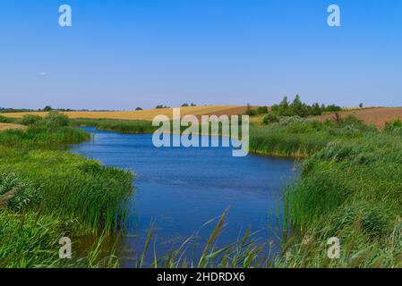Fluss mit üppig grünen Ufern schlängelt sich durch Ackerland mit Feldern, die für Getreideanbau gepflanzt und für die neue Ernte in einer landschaftlich reizvollen Landwirtschaft gepflügt wurden Stockfoto