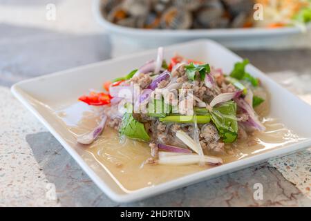 Yum Woonsen oder würziger und saurer Salat aus Vermicelli oder Glasnudel mit gehacktem Schweinefleisch und Pflanzenkräutern, Close Up gesundes Thai-Essen auf weißem Teller auf Stein Stockfoto