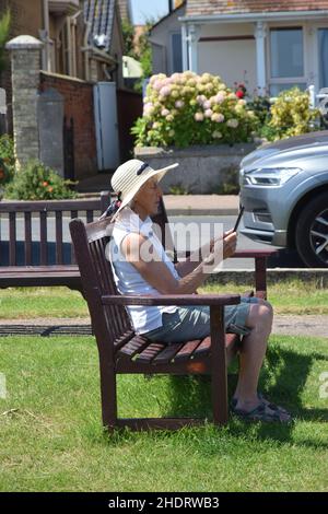 Ältere Frauen sitzen auf einer Bank und lesen eBook Stockfoto