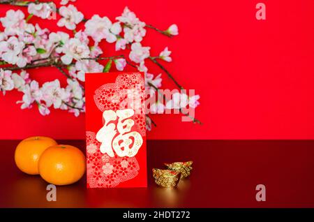 Rotes Umschlagpaket oder ang bao (Wort bedeuten Reichtum) legt mit Orangen und Barren mit Pfirsichblüte auf roten Glitzerpapier Hintergrund. Stockfoto