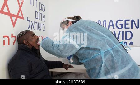 Jerusalem, Israel. 6th Januar 2022. Ein Sanitäter des Magischen David Adom, des nationalen medizinischen Notdienstes Israels, Sammelt eine Abstrichprobe eines israelischen Mannes der Beta-Israel-Gemeinschaft, auch bekannt als äthiopische Juden, an einer mobilen COVID-19-Teststation, da Israel als erstes Land der Welt am 6. Januar 2022 in Jerusalem, Israel, eine vierte COVID-19-Impfkampagne gestartet hat. Israel begann, Menschen über 60 Jahren und im Gesundheitswesen vierte Dosen des Pfizer-Coronavirus-Impfstoffs zu verabreichen, als Teil der Bemühungen, die rasch steigenden Infektionsraten, die durch den Omicr verursacht wurden, einzudämmen Stockfoto