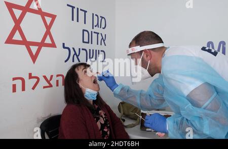 Jerusalem, Israel. 6th Januar 2022. Ein Sanitäter des Magischen David Adom, Israels nationaler Notarzt, sammelt eine Abstrichprobe einer israelischen Frau an einer mobilen COVID-19-Teststation, während Israel als erstes Land der Welt am 6. Januar 2022 in Jerusalem, Israel, eine vierte Impfkampagne gegen COVID-19 einführt. Israel begann damit, Menschen über 60 Jahren und im Gesundheitswesen vierte Dosen des Pfizer-Coronavirus-Impfstoffs zu verabreichen, als Teil der Bemühungen, die durch die Omicron-Variante rasch steigenden Infektionsraten einzudämmen. Kredit: Eddie Gerald/Alamy Live Nachrichten Stockfoto