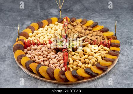 Mischmuttern Platte auf dunklem Hintergrund. Snack-Teller mit Haselnüssen, Pistazien, Cashews, Mandeln und getrockneten Aprikosen zubereitet. Horizontale Ansicht. Nahaufnahme Stockfoto