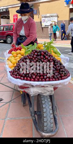 Cuenca, Ecuador, 24. Dez 2021 - eine Frau verkauft Kirschen und Früchte von einer Schubkarre. Stockfoto