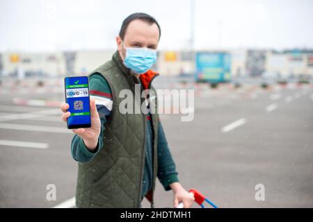 Mann mit Covid Zertifikat auf dem Smartphone, die ihm erlauben, Waren zu kaufen Stockfoto