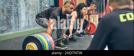 Gemischtes Team, das mit dem Trainer Gewichte im Fitnessstudio hebt Stockfoto