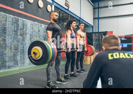 Gemischtes Team, das mit dem Trainer Gewichte im Fitnessstudio hebt Stockfoto