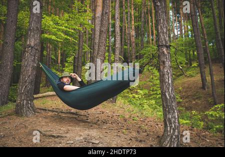 Mann, der in einer Hängematte am Waldrand steht und die Landschaft bewundert Stockfoto