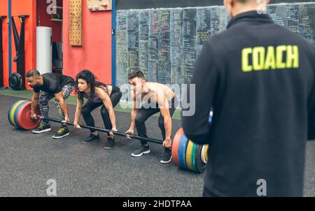 Gemischtes Team, das mit dem Trainer Gewichte im Fitnessstudio hebt Stockfoto