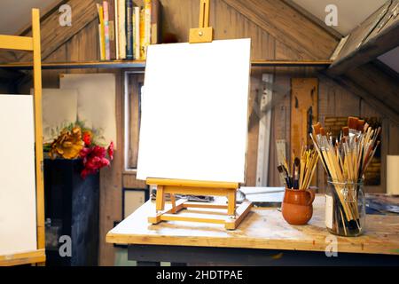 Künstlerische Ausrüstung in einem Künstleratelier: Leere Künstlerleinwand auf HolzStaffelei und Pinsel Retro getönte Foto-Kopierfläche Stockfoto