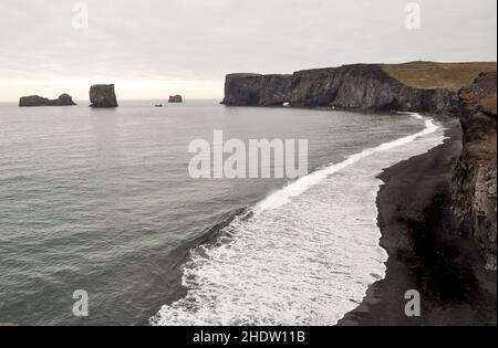 Blick auf den leeren, schwarzen Sandstrand von Reynisfjara und die Felsformationen an einem grauen Tag, an dem die weiße Brandung am Ufer zusammenbricht - Vik, Island Stockfoto