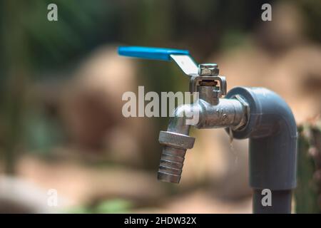 Metall Wasserhahn Hahn Edelstahl Wasserhahn Hebel Kugelhahn blauen Griff an Adapter Manatee Rohr verbunden. Hintergrund verwischen. Gartenarbeit in der Natur Stockfoto