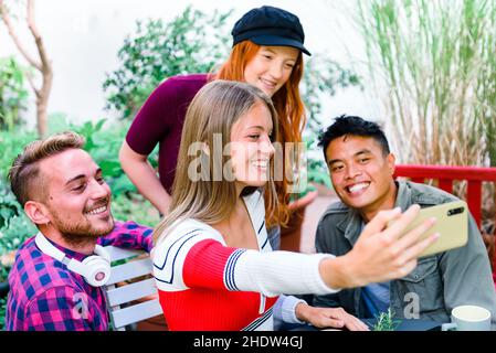 Eine multikulturelle Gruppe glücklicher junger Freunde, die zusammen auf einem Mobiltelefon ein Selfie machen, lachen und lächeln, während sie als Gruppe im Freien posieren Stockfoto