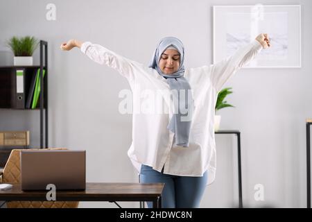 Frau In Hijab Steht Und Dehnt Sich Vor Dem Computer Stockfoto